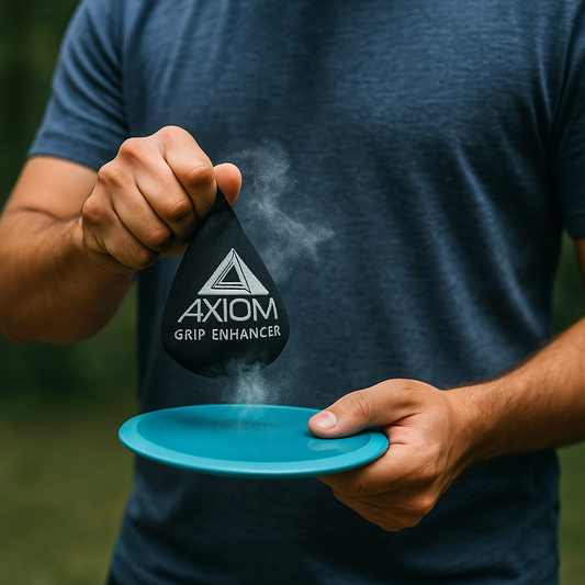 Disc golfer holding an Axiom grip bag in one hand and an Axiom disc in the other, with a visible chalk-like puff coming from the bag to show grip dust effec